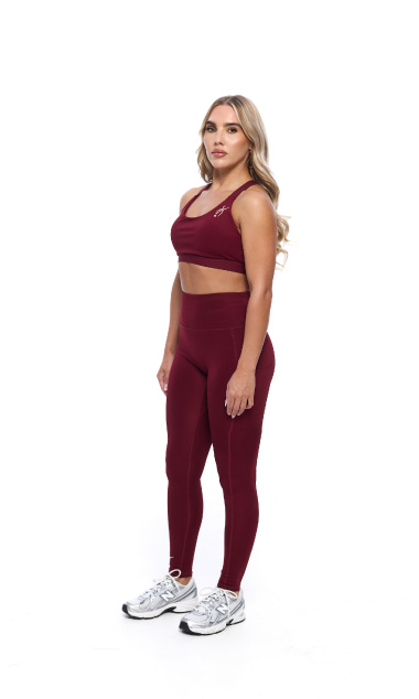 Female wearing Burgandy leggings and matching bra standing in front of a white background