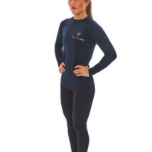 Blonde-haired female model wearing a blue sports base layer, matching blue leggings, and white trainers, standing in front of a white wall with hands on her hips.