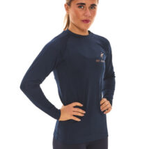 Blonde-haired female model wearing a blue sports base layer, matching blue leggings, and white trainers, standing in front of a white wall with hands on her hips.