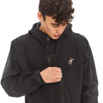 Male model with black hair wearing a black rain jacket, looking at the jacket logo against a white wall.