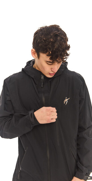 Male model with black hair wearing a black rain jacket, looking at the jacket logo against a white wall.