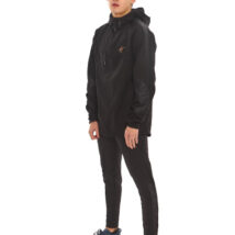 Male with black hair wearing black tracksuit bottoms and black rain jacket standing in front of a white wall