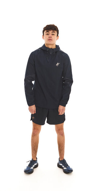 Male model with black hair wearing blue rain jacket and blue shorts standing against a white wall.