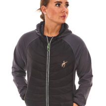 Brown-haired woman in black athletic quarter-zip and black shorts standing against a white wall.