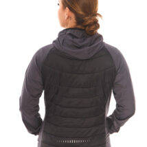 Rear view of brown-haired woman in black athletic quarter-zip and shorts standing against a white wall.