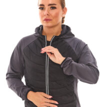 Brown-haired woman in black athletic quarter-zip and black shorts standing against a white wall.