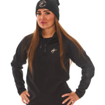 Brown-haired woman in black athletic tracksuit top and base layer bottoms standing against a white wall with hands on hips.