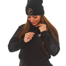 Brown-haired woman in black athletic tracksuit top and base layer bottoms standing against a white wall with hands on hips.