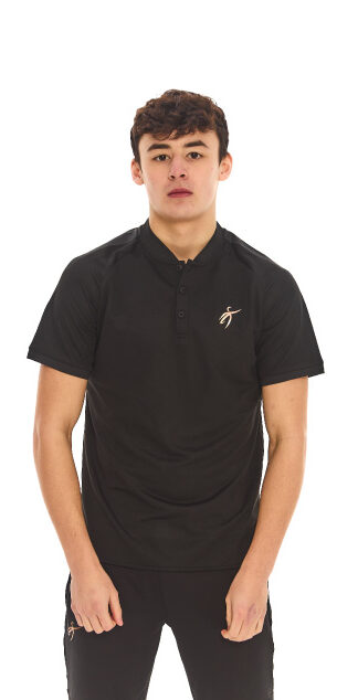 Male model with black hair wearing a black polo shirt and black tracksuit bottoms, standing against a white wall.