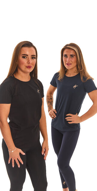 Two females, one wearing black and one wearing blue base layers. One with blonde hair and one with brown hair standing in front of a white wall.