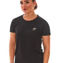 Brown-haired female model wearing black sports base layers, black leggings, and black trainers, standing in front of a white wall with hands on her hips.