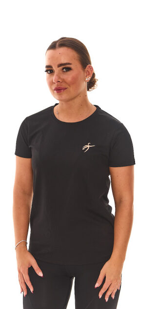 Brown-haired female model wearing black sports base layers, black leggings, and black trainers, standing in front of a white wall with hands on her hips.