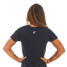 Rear view of blonde female model wearing blue sports base layers, standing against a white wall with hands on hips.